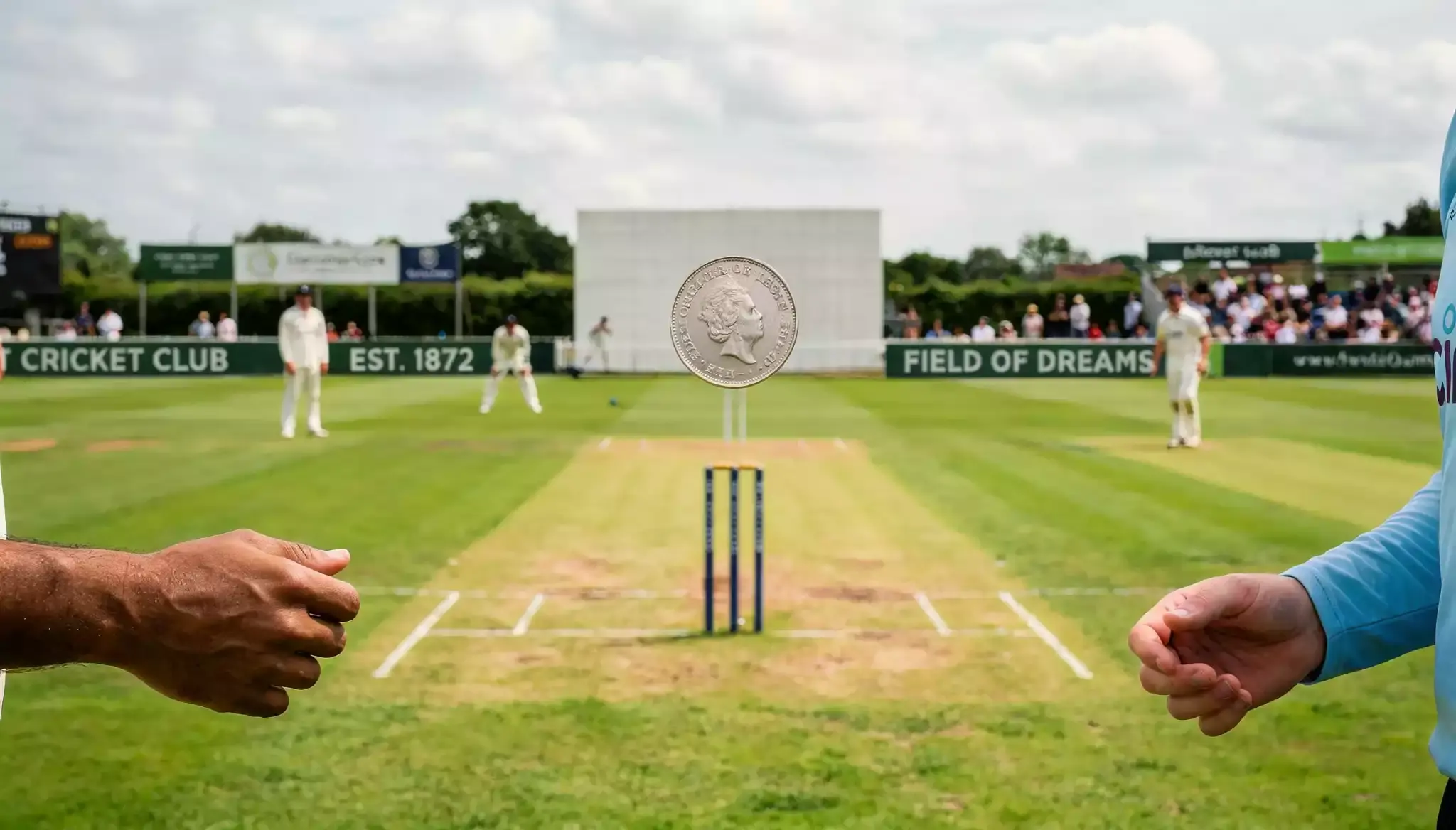 Silver coin spinning in mid-air during a cricket toss with pitch in background